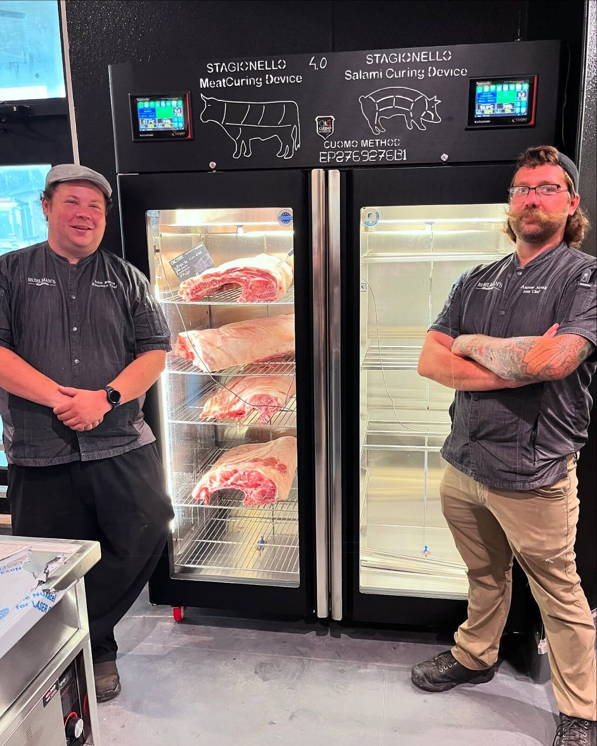 Chef John Benton and his sous chef beside a black Stagionello 4.0 Meat and Salami Curing Device TWIN loaded with pork loins